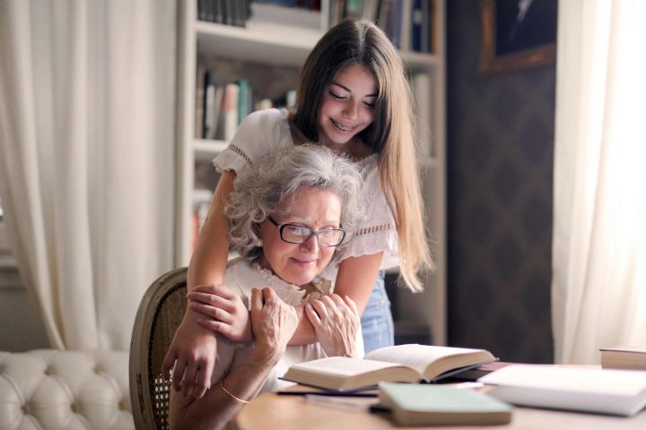 A heartwarming moment of a granddaughter embracing her grandmother as she reads a book together indoors.